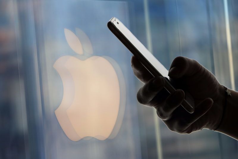 --FILE--A Chinese man uses his iPhone smartphone in front of a logo of Apple in Shanghai, China, 16 December 2018. Apple Inc. Wednesday cut its revenue expectations for the most recent quarter, citing slower sales in China. The iPhone maker estimated revenue of about $84 billion for the quarter ended Dec. 29, down from a previous projection of $89 billion to $93 billion. In a letter to investors, Apple Chief Executive Officer Tim Cook attributed the reduction to a slowdown in the Greater China region, which accounts for almost 20% of its revenue. 