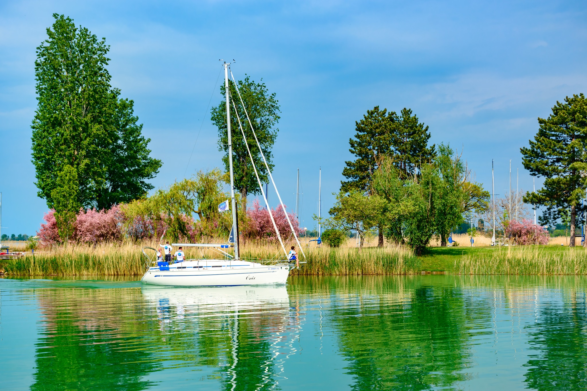 Nyaralóhangulat a Balatonnál: azúrkék tó, harsogó zöldek a parton, andalgó turisták az utakon